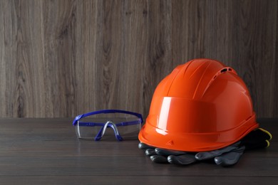 Hard hat, goggles and gloves on wooden table, space for text. Safety equipment