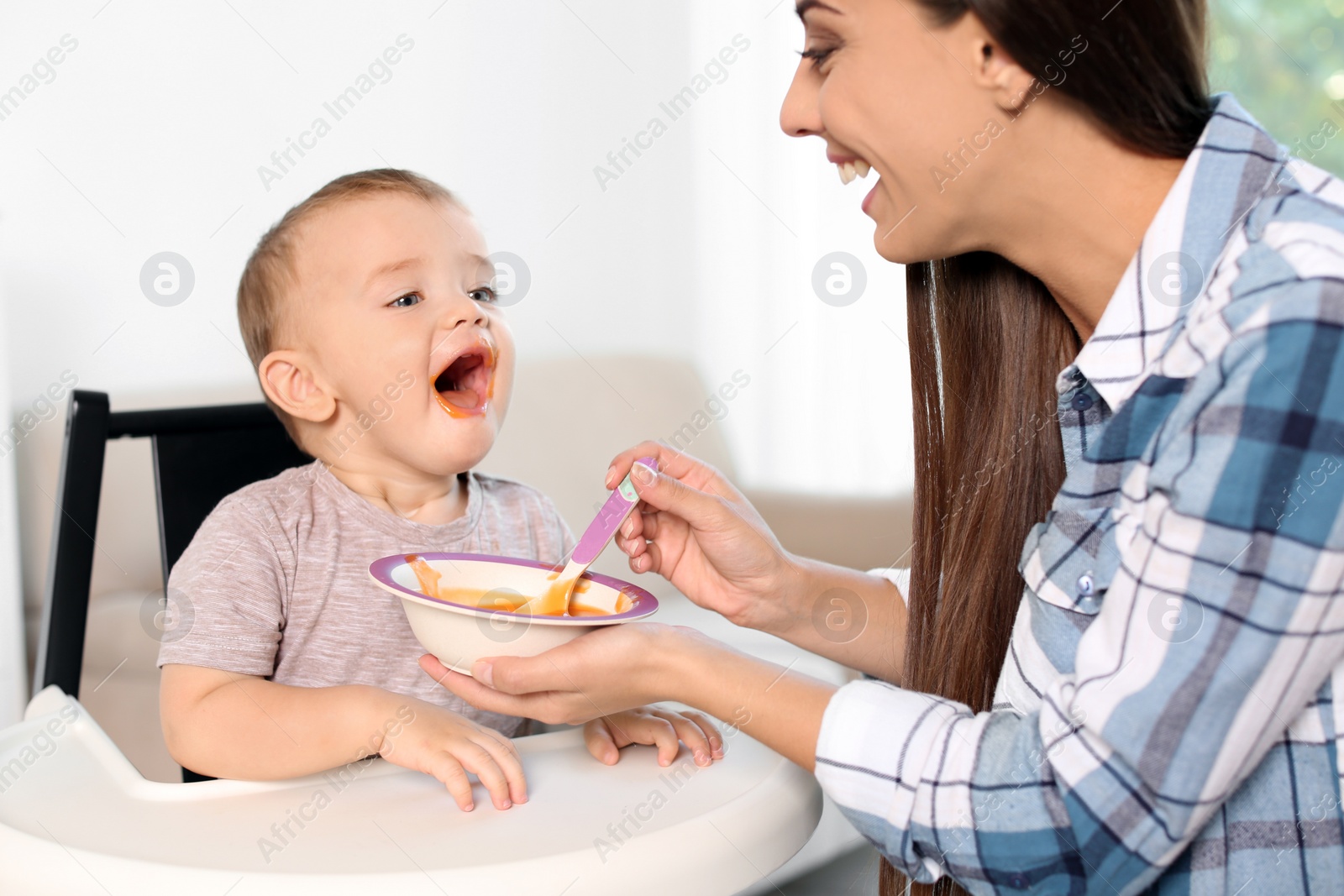 Photo of Woman feeding her child in highchair indoors. Healthy baby food