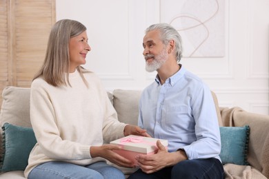 Happy affectionate senior couple with gift box on sofa indoors