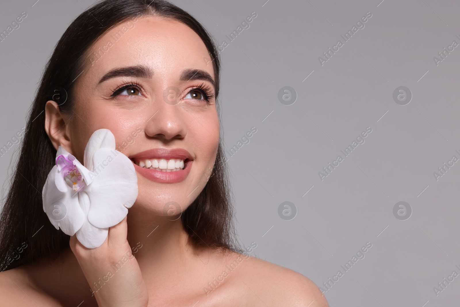 Photo of Portrait of smiling woman with orchid flower on grey background. Space for text