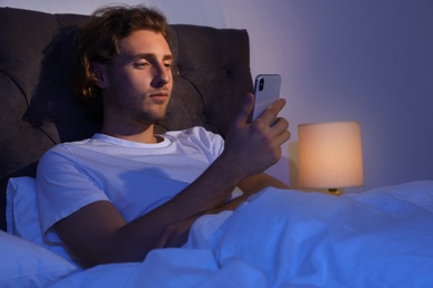 Handsome young man using smartphone in dark room at night. Bedtime