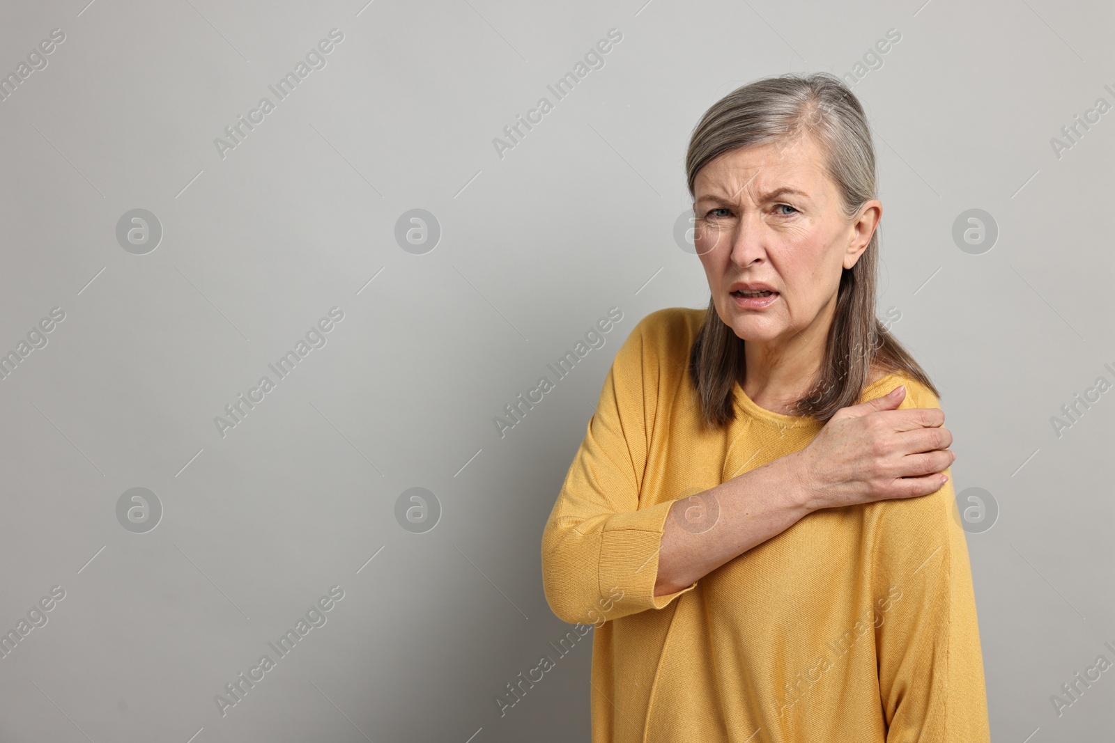 Photo of Arthritis symptoms. Woman suffering from pain in shoulder on gray background, space for text