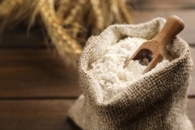 Photo of Sack of flour with wooden scoop on table, closeup. Space for text