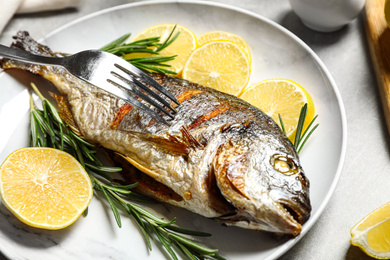 Photo of Delicious roasted fish with lemon on grey table, closeup