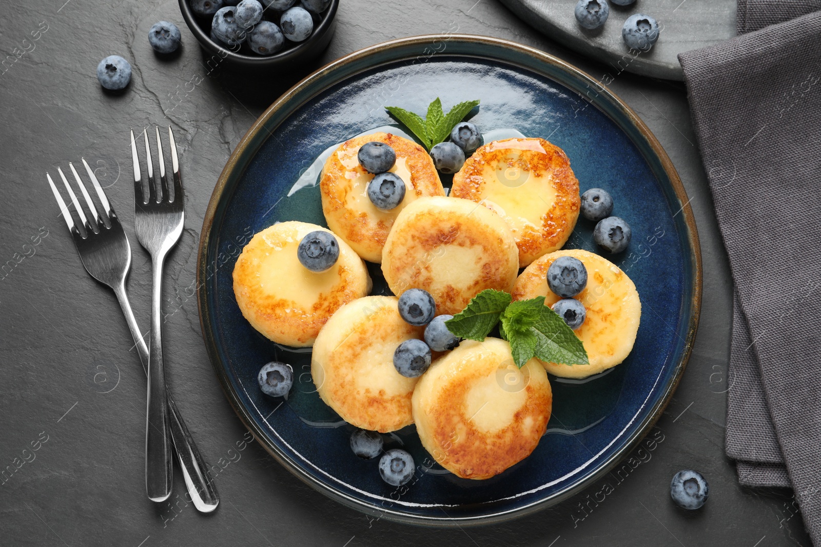 Photo of Delicious cottage cheese pancakes with blueberries on black table, flat lay