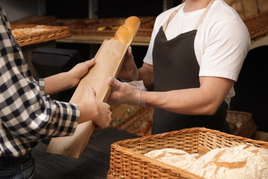 Photo of Woman buying fresh baguette in bakery shop, closeup