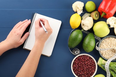 Woman developing diet plan at blue wooden table with products and measuring tape, top view