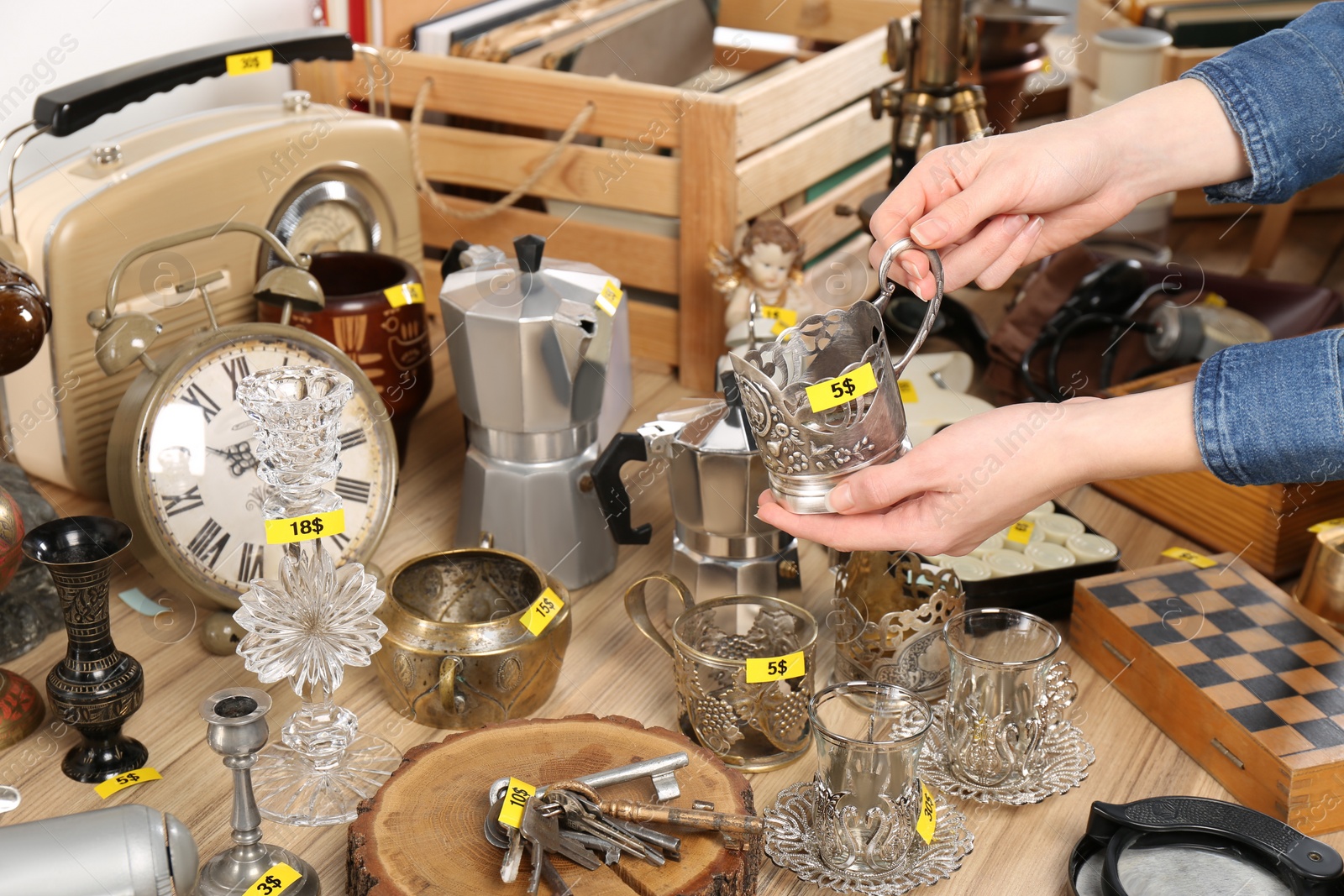 Photo of Woman holding vintage metal cup near table with different stuff, closeup. Garage sale