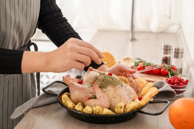 Photo of Woman cooking Chicken with orange and potato slices at wooden table, closeup