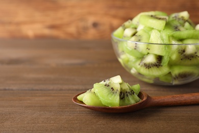 Photo of Spoon with kiwi slices on wooden table. Space for text