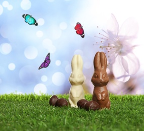 Image of Chocolate bunnies and eggs on green grass outdoors. Easter celebration