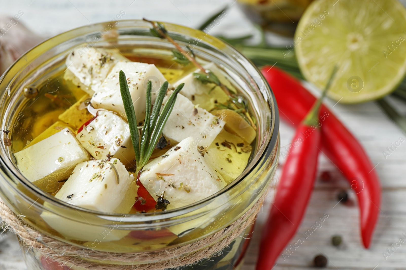 Photo of Pickled feta cheese in jar on white wooden table, closeup