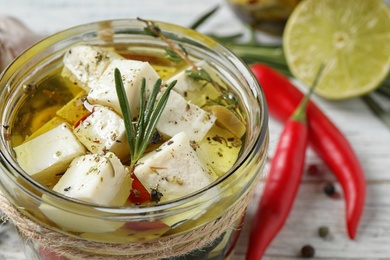 Pickled feta cheese in jar on white wooden table, closeup