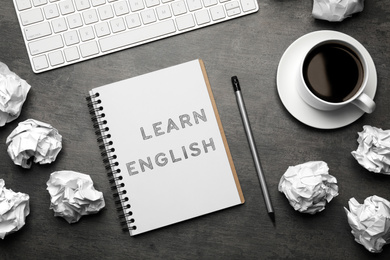 Notebook with text Learn English, keyboard and crumpled paper balls on grey table, flat lay