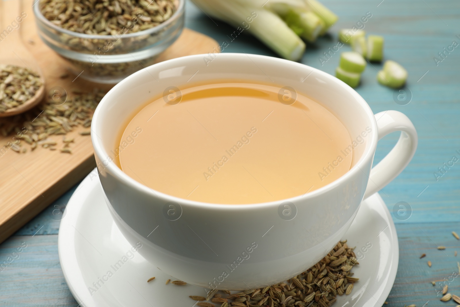 Photo of Fennel tea in cup, seeds and fresh vegetable on light blue wooden table, closeup