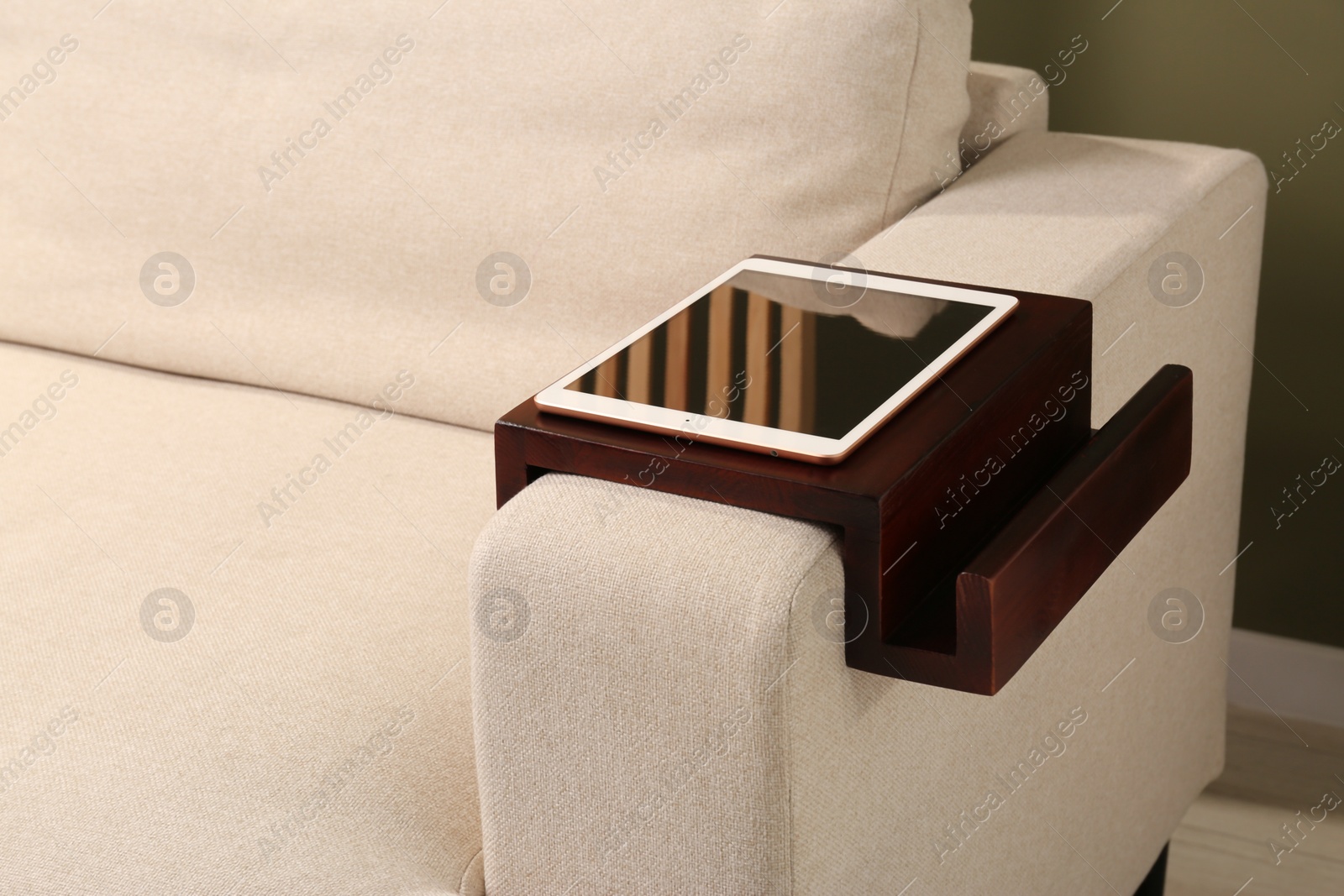 Photo of Tablet on sofa armrest wooden table in room. Interior element