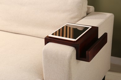 Tablet on sofa armrest wooden table in room. Interior element