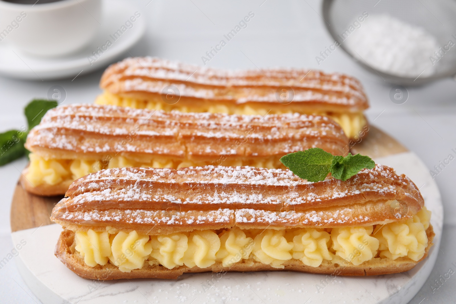 Photo of Delicious eclairs filled with cream and mint on table, closeup