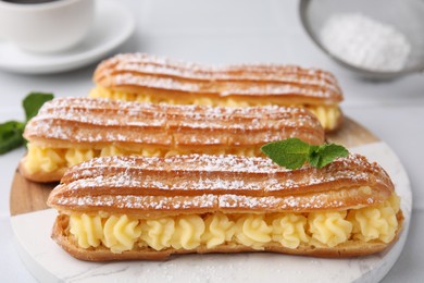 Photo of Delicious eclairs filled with cream and mint on table, closeup