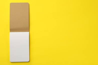 Stylish open notebook with blank sheets on yellow background, top view. Space for text