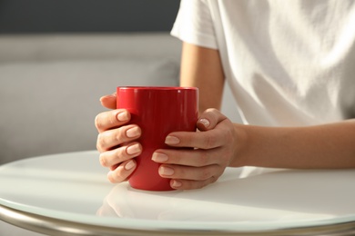 Woman with red cup at table indoors, closeup