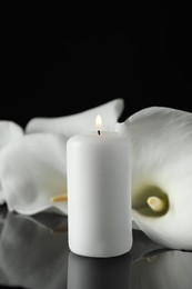 Burning candle and white calla lily flowers on black mirror surface in darkness, closeup with space for text. Funeral symbol