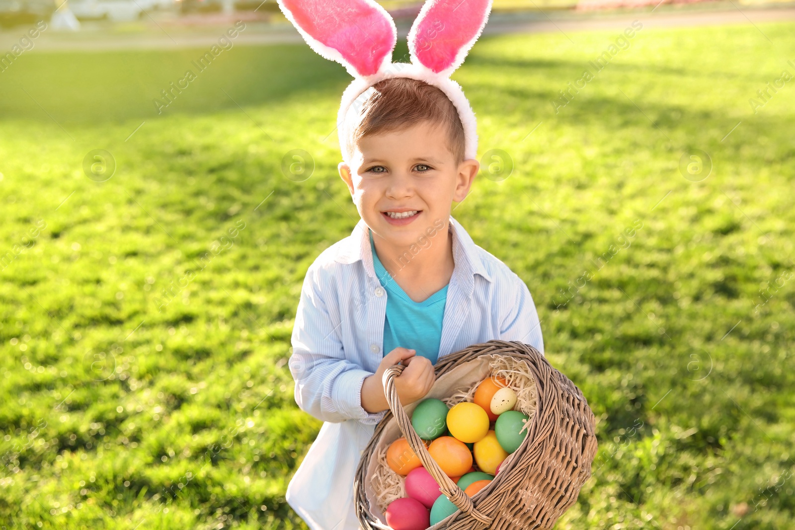 Photo of Cute little boy with bunny ears and basket of Easter eggs in park