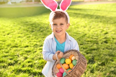 Cute little boy with bunny ears and basket of Easter eggs in park