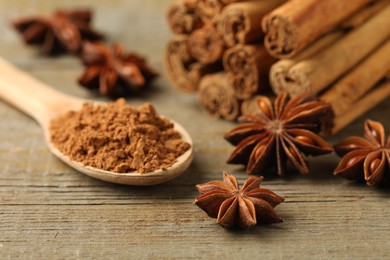 Spoon with cinnamon powder, sticks and star anise on wooden table, closeup
