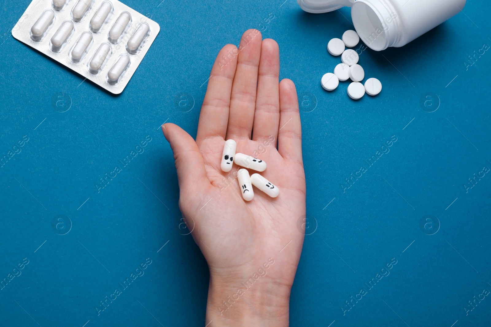 Photo of Woman holding antidepressants with different emoticons on blue background, top view
