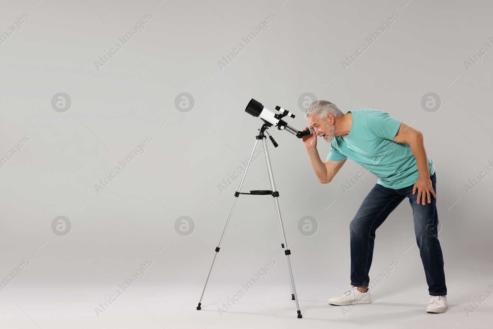 Photo of Senior astronomer looking at stars through telescope on grey background. Space for text