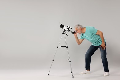 Senior astronomer looking at stars through telescope on grey background. Space for text