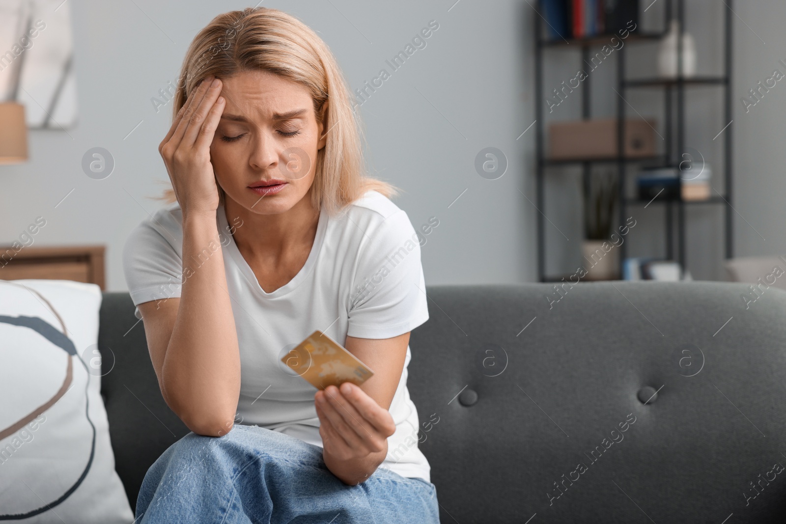 Photo of Stressed woman with credit card on sofa at home, space for text. Be careful - fraud