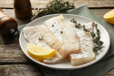 Photo of Fresh raw cod fillets with thyme and lemon on wooden table