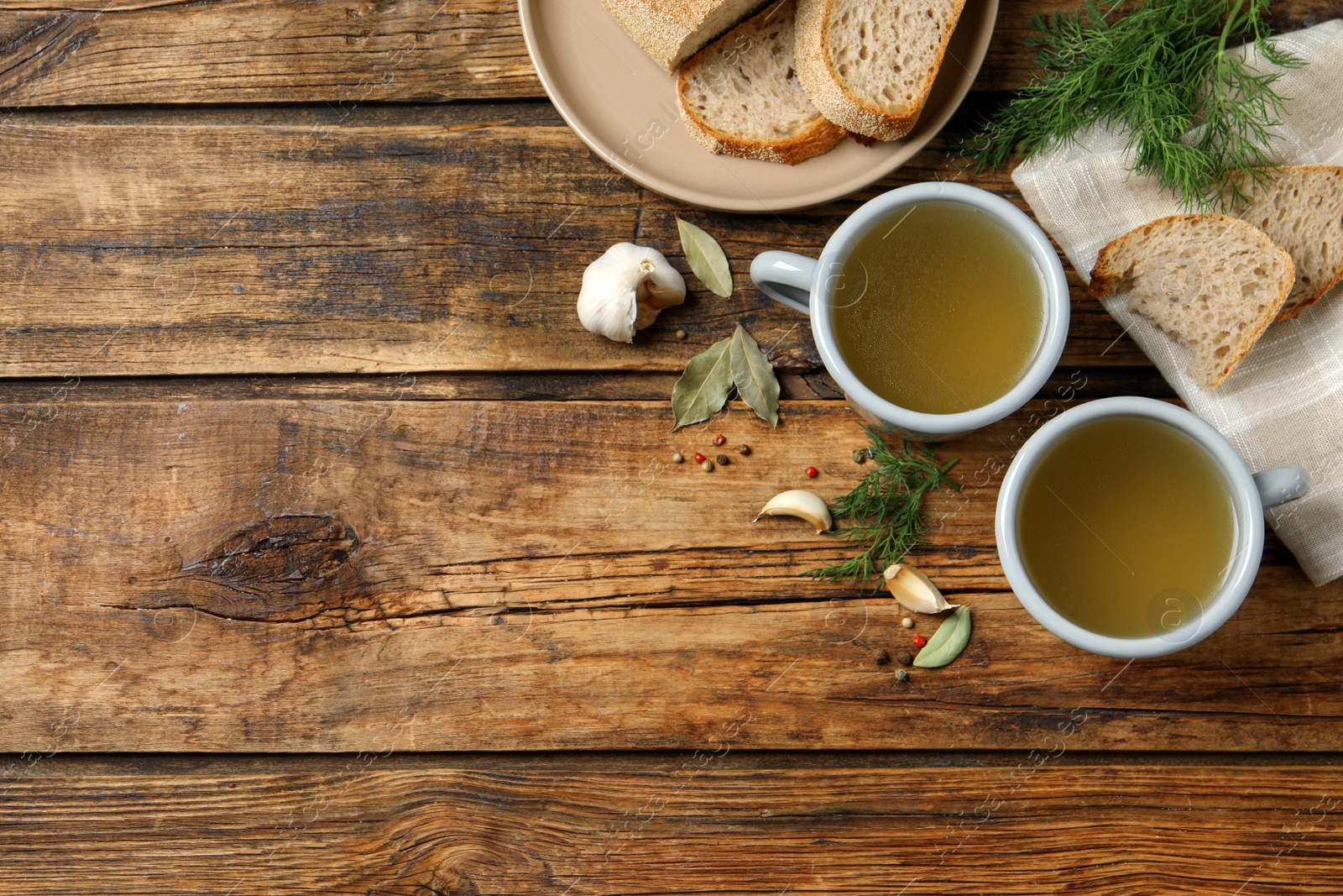 Photo of Hot delicious bouillon in cups on wooden table, flat lay. Space for text