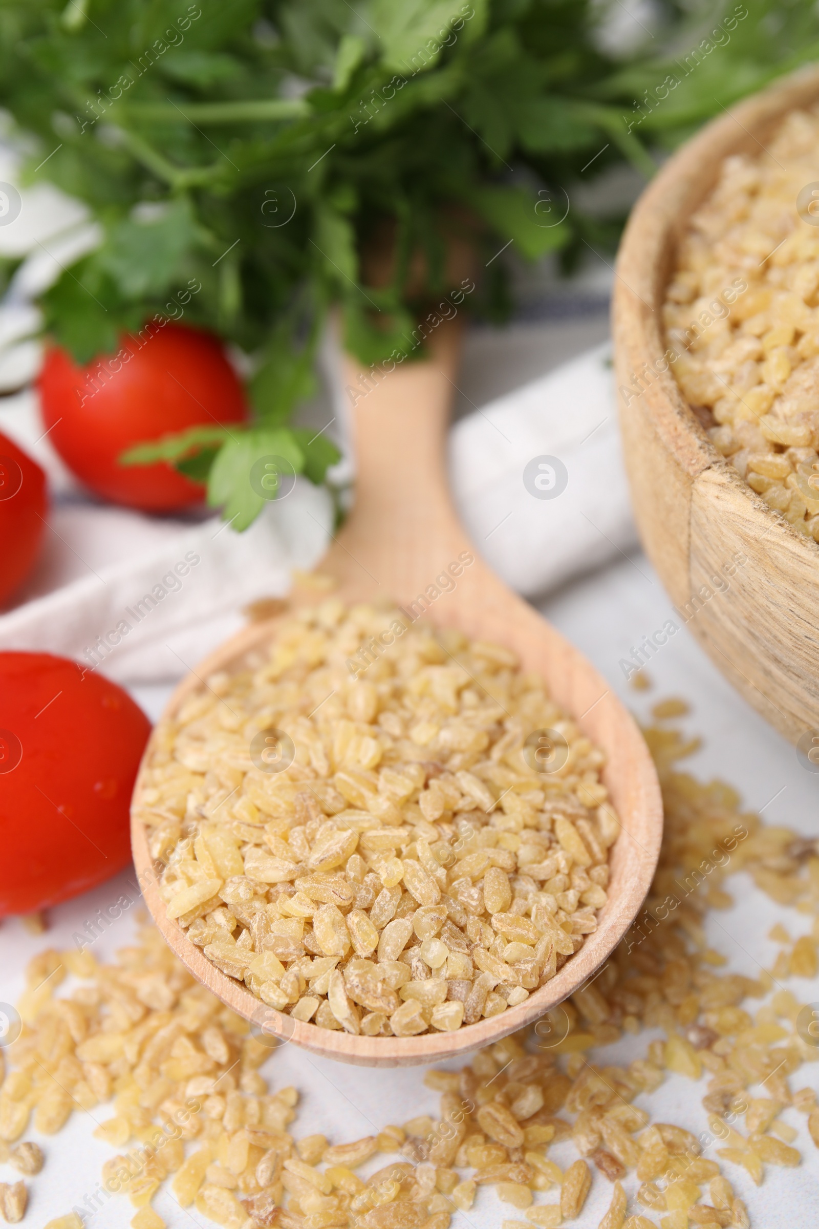 Photo of Spoon with raw bulgur and tomatoes on table, closeup
