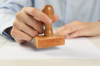 Woman stamping blank sheet of paper at white wooden table, closeup