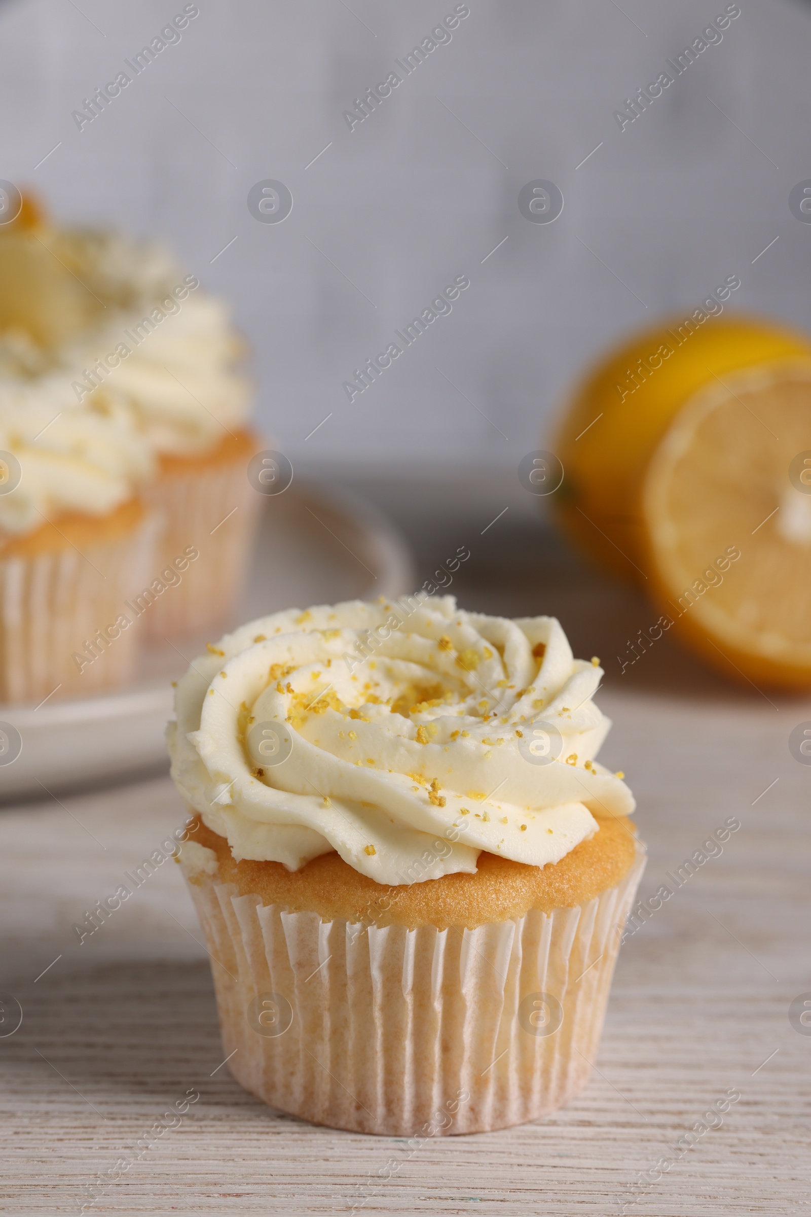 Photo of Delicious cupcake with white cream and lemon zest on light wooden table, closeup