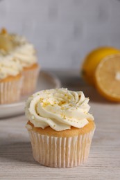 Photo of Delicious cupcake with white cream and lemon zest on light wooden table, closeup