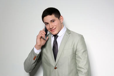 Portrait of young businessman talking on phone against light background