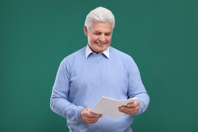 Photo of Portrait of senior teacher with paper at green chalkboard
