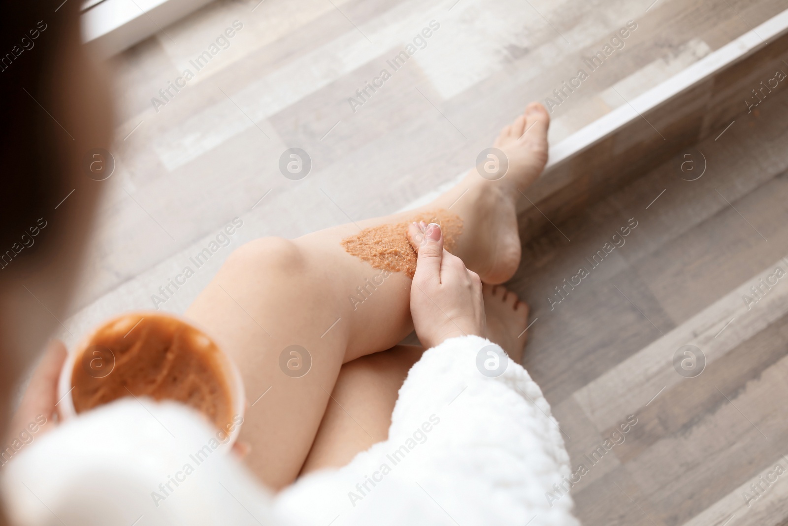 Photo of Young woman applying natural scrub onto her skin in bathroom