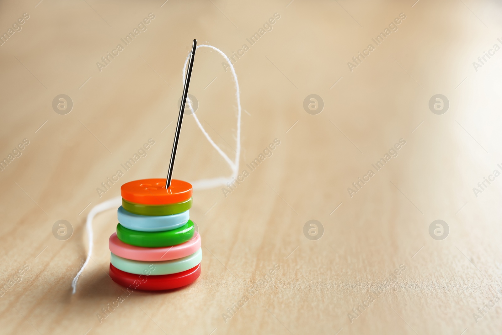 Photo of Needle with thread and buttons for tailoring on wooden background