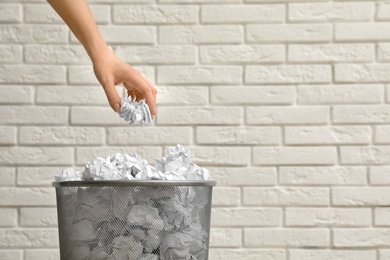 Photo of Woman throwing crumpled paper into metal bin against brick wall, closeup. Space for text