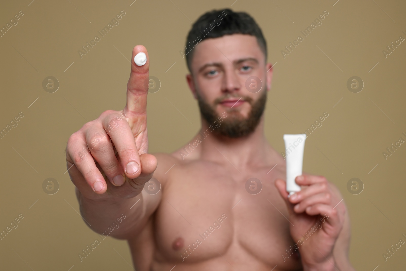 Photo of Handsome man with tube of body cream on pale brown background, selective focus