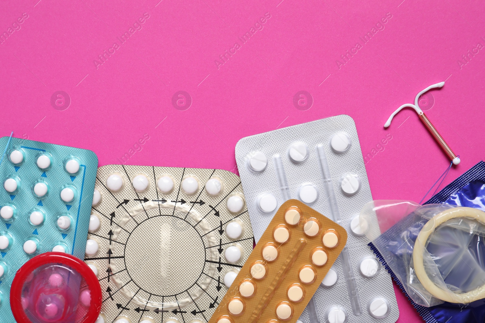 Photo of Contraceptive pills, condoms and intrauterine device on pink background, flat lay with space for text. Different birth control methods