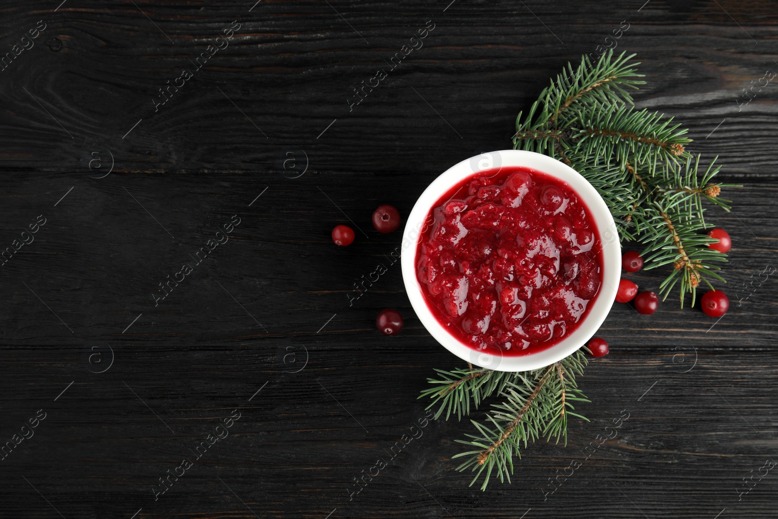 Photo of Bowl of cranberry sauce with fir tree branches on wooden background, flat lay. Space for text