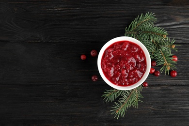 Photo of Bowl of cranberry sauce with fir tree branches on wooden background, flat lay. Space for text