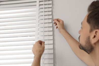 Photo of Worker opening or closing horizontal window blind indoors, closeup