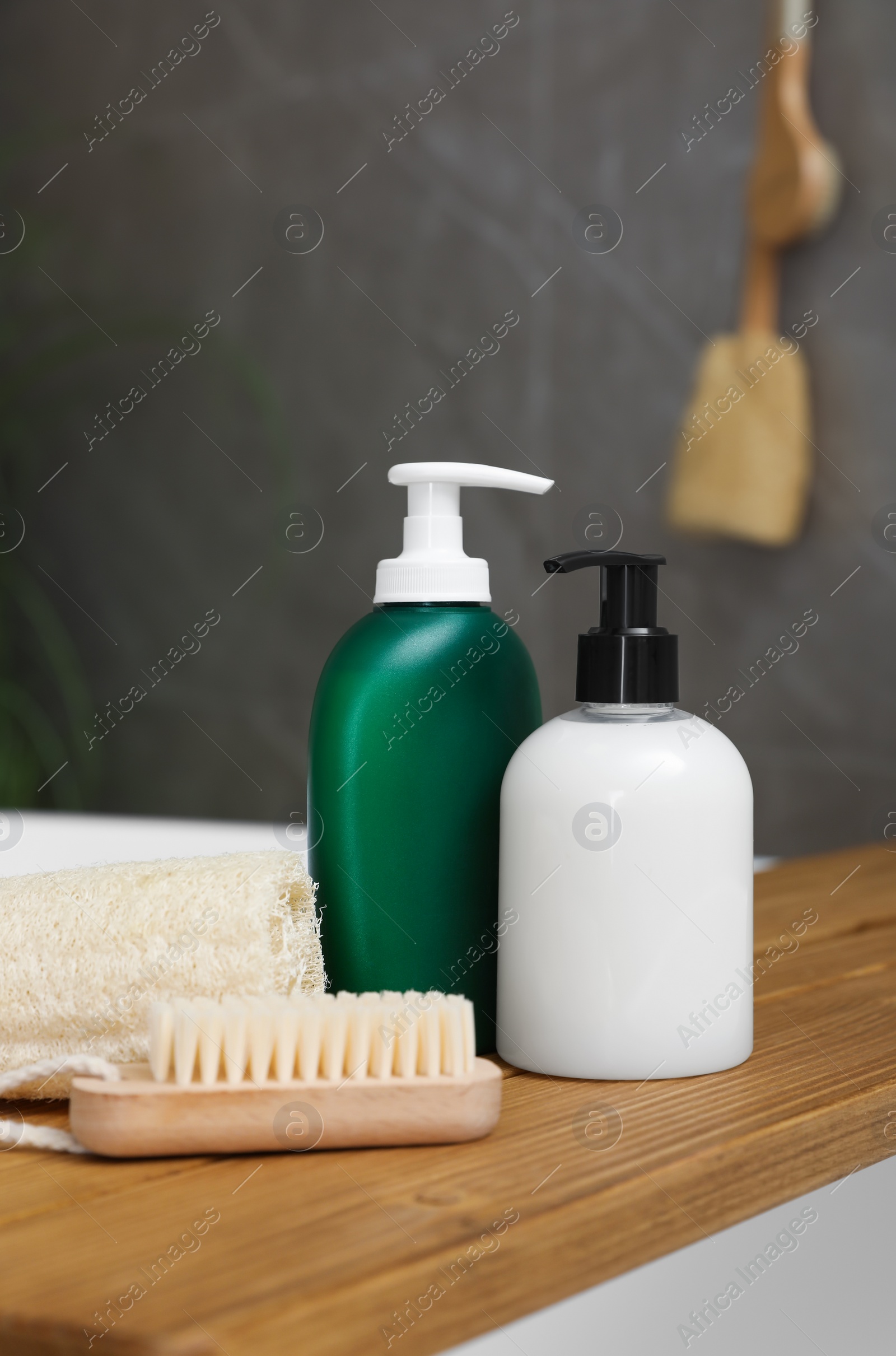 Photo of Wooden bath tray with bottles of shower gels, loofah and brush on tub indoors